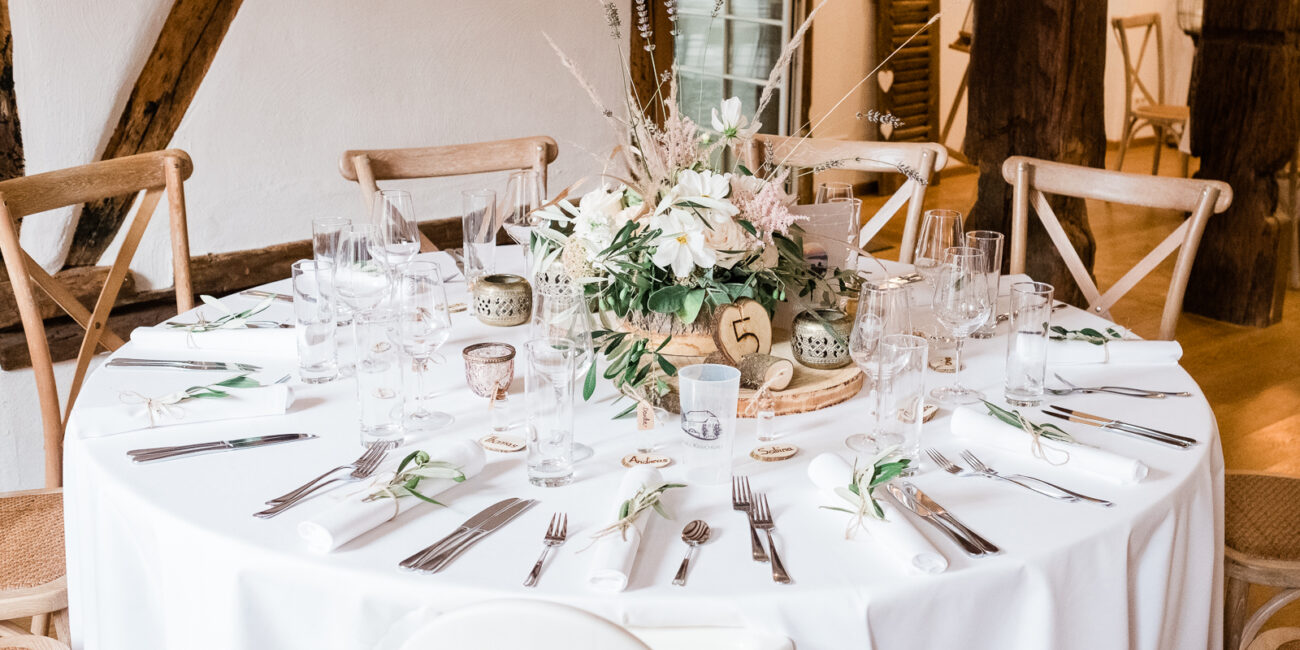 Dekorierter und gedecker Hochzeitstisch mit Blumeerrangement in der Mitte des Tisches
