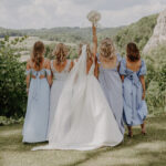 Braut in weißem Kleid und Schleier mit Bridemaids in blauen Kleidern auf der Wiese am Hofgut Maisenburg