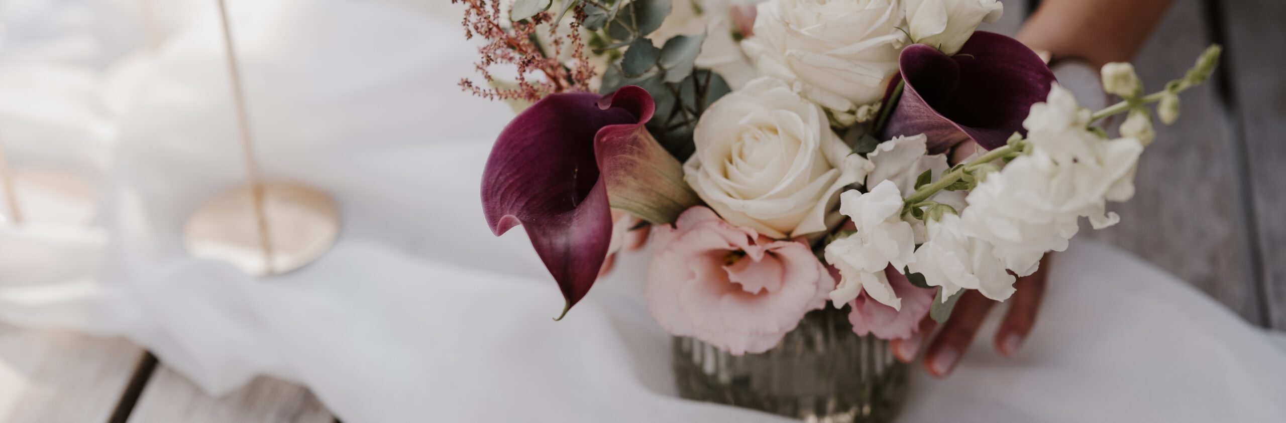 Weiße, rosane und weinrote Blumen in Vase auf einem weißen Dekostoff