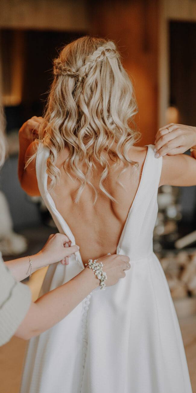 Braut beim Anziehen ihres Brautkleids von hinten. Großer Rückenausschnitt