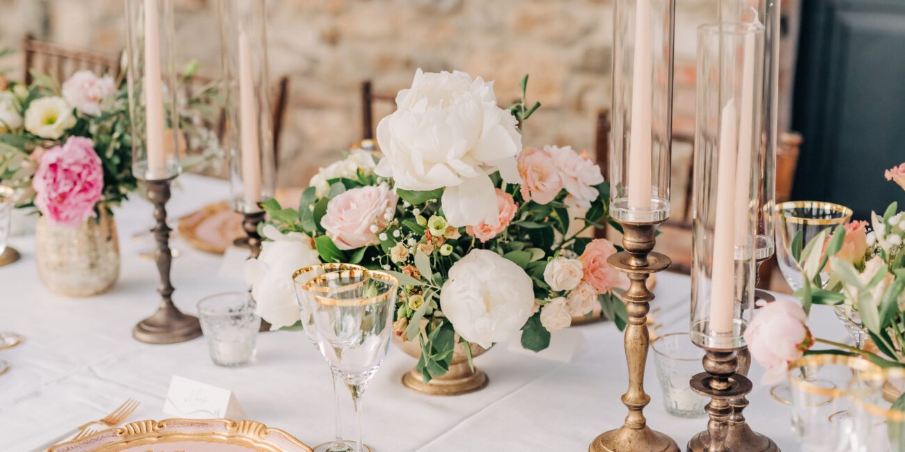 Dekorierter Hochzeitstisch mit goldenen Kerzenständern und Tellern und ein Blumenerrangement in Pastellfarben