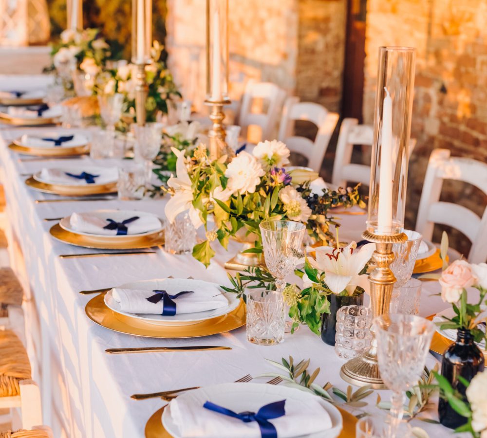 gedeckte Hochzeitstafel mit weißer Tischdecke, goldene Unterteller, Kerzen und Blumen